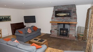 A living room with grey sofas, a fireplace, a television, and a painting on the wall. - Auchendennan Farm Cottage - sleeps 6 guests  in 3 bedrooms (Alexandria)
