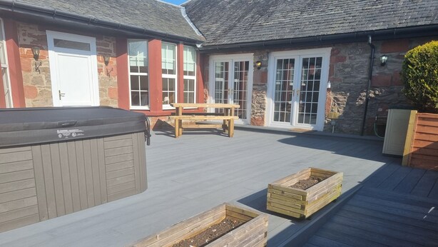 A patio area with a hot tub, wooden planters, and a wooden table. - Auchendennan Farm Cottage - sleeps 6 guests  in 3 bedrooms (Alexandria)