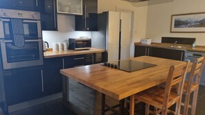 A modern kitchen with a built-in oven, microwave, and a wooden dining table with chairs. - Auchendennan Farm Cottage - sleeps 6 guests  in 3 bedrooms (Alexandria)
