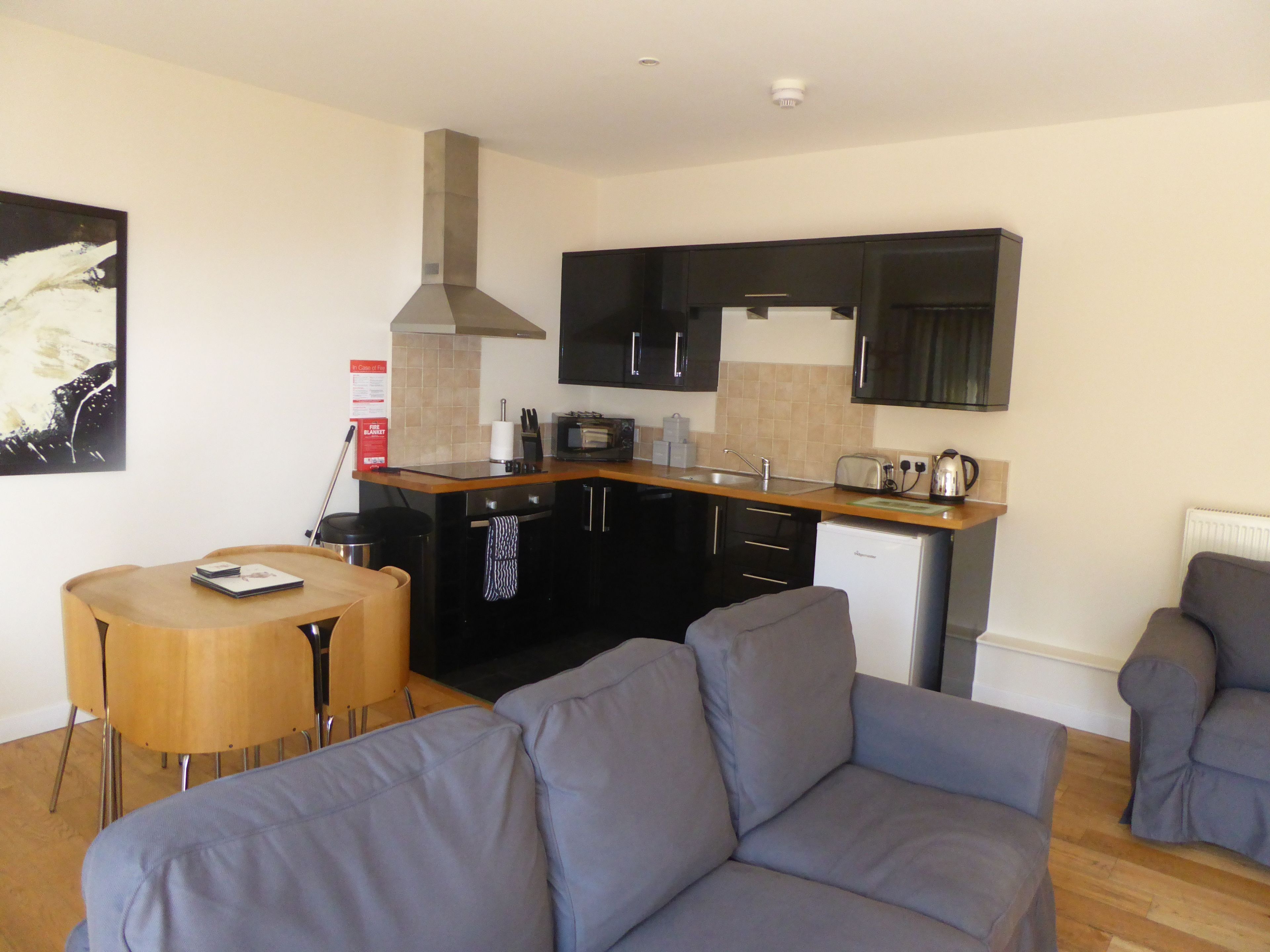 A compact living space with a kitchenette, grey sofa, and a small dining table.