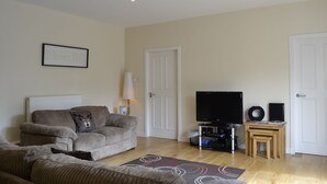A living room with a sofa, a television, a small table, and a lamp. - Courtyard Studio (Auchendennan) (Alexandria)