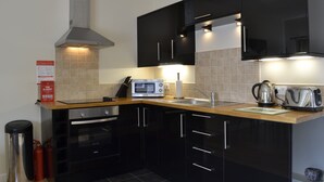 A modern kitchen with black cabinets, a stainless steel range hood, a microwave, a kettle, and a toaster. - Courtyard Studio (Auchendennan) (Alexandria)