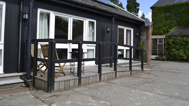 A black building with white windows and a wooden deck. - Courtyard Studio (Auchendennan) (Alexandria)