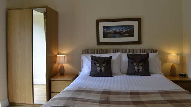 A hotel room with a bed, two pillows, a nightstand, a lamp, a framed picture on the wall, and a wardrobe. - Ivy Garden Cottage ( Auchendennan ) - sleeps 2 guests  in 0 bedrooms (Alexandria)