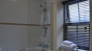 A modern bathroom with a glass-enclosed shower, a white bathtub, and a window with blinds. - Ivy Garden Cottage ( Auchendennan ) - sleeps 2 guests  in 0 bedrooms (Alexandria)
