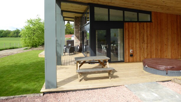 A covered outdoor area with a wooden deck, a table, and a bench. - Oak Lodge (Auchendennan) - sleeps 4 guests  in 2 bedrooms (Alexandria)