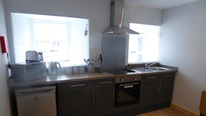 A modern kitchen with a dishwasher, oven, and a stainless steel range hood. - The Stables Lower Cottage 5 (Auchendennan) - sleeps 2 guests  in 1 bedroom (Alexandria)