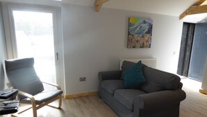 Un salon moderne avec un canapé gris, une table basse en bois et un fauteuil. Il y a un tableau au mur et une fenêtre avec des stores.