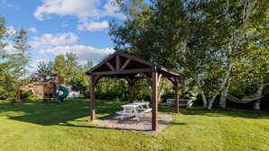 A gazebo with a picnic table in a grassy park area with trees and playground equipment in the background. - Sand Dune Cottage, 2 BRs, Kitchen, living and a patio (York)