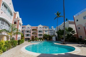 A resort with a central swimming pool, multiple balconies, and palm trees. - Cozy 1 BR apartment with AC and WiFi, walking distance to the beach in Bavaro (Punta Cana)