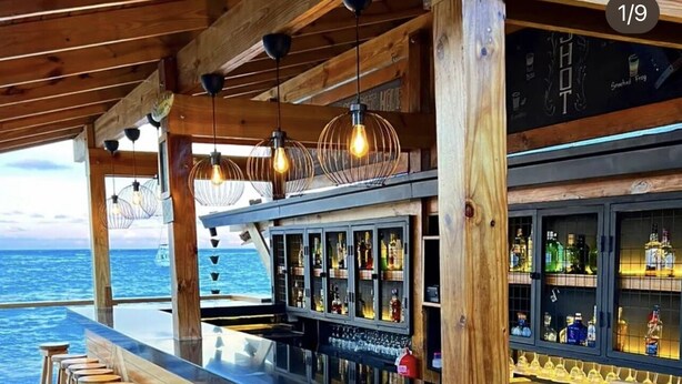 A wooden deck bar with stools, a bar counter, and a view of the ocean. - Cozy 1 BR apartment with AC and WiFi, walking distance to the beach in Bavaro (Punta Cana)