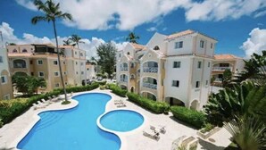 A resort with a large swimming pool, multiple buildings with balconies, and palm trees. - Cozy 1 BR apartment with AC and WiFi, walking distance to the beach in Bavaro (Punta Cana)