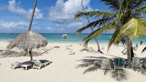 A beach with white sand, palm trees, and a thatched umbrella. - Cozy 1 BR apartment with AC and WiFi, walking distance to the beach in Bavaro (Punta Cana)