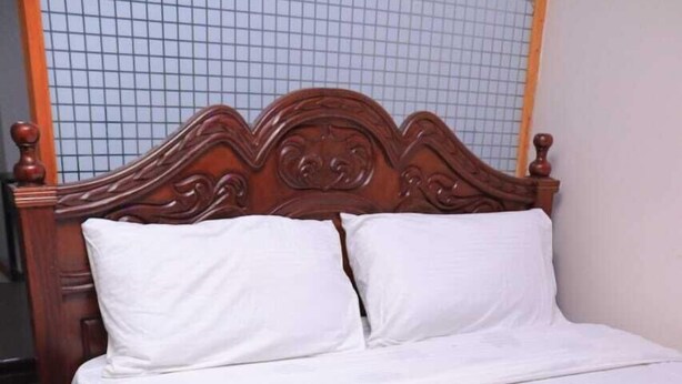 A neatly made bed with a wooden headboard and white bedding in a room with a blue carpet. - Beautiful 1-Bed Apartment in Nairobi (Nairobi)