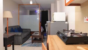A compact living space with a sofa, a small table, a kitchen area with a stove, and a refrigerator. - Beautiful 1-Bed Apartment in Nairobi (Nairobi)