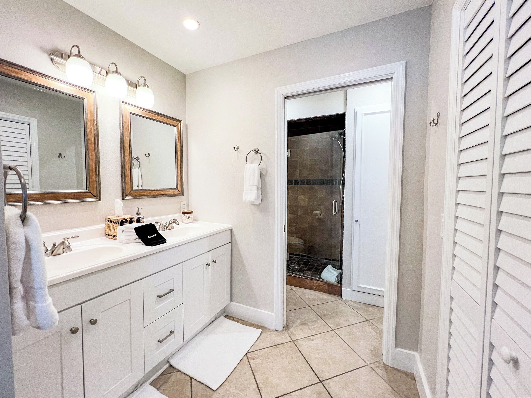 Une salle de bain avec un meuble-lavabo blanc, deux miroirs, un porte-serviettes et un espace douche.