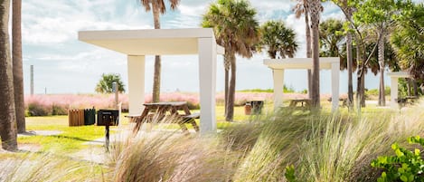 A gazebo structure with picnic tables, surrounded by tall palm trees and grass.