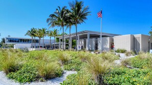 A modern building with a covered walkway, palm trees, and an American flag. - 100' from Point of Rocks, Elegant 3BR Siesta Key Beach Retreat (Sarasota)