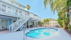 Un espace piscine agrémenté d’un escalier blanc menant à un balcon, entouré de mobilier d’extérieur et de palmiers.