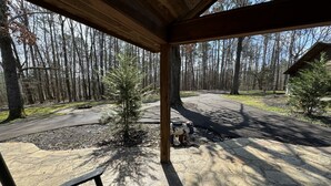 A covered outdoor area with a stone patio, a small tree, and a bench.