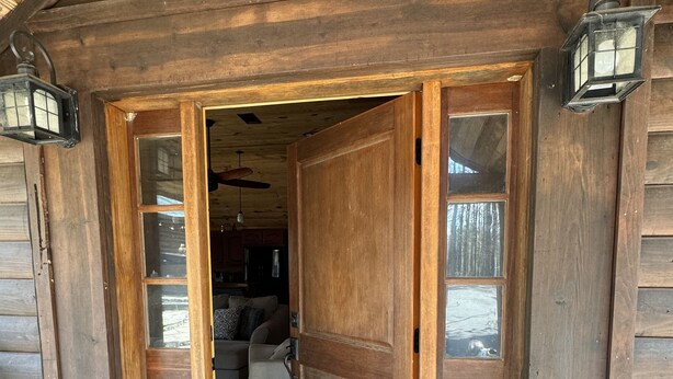 A wooden cabin entrance with a large door, a doormat, and two lanterns.
