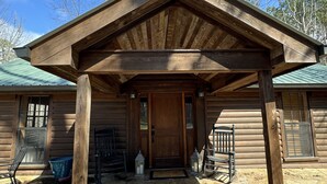 A wooden cabin with a covered porch, stone flooring, and a green roof.