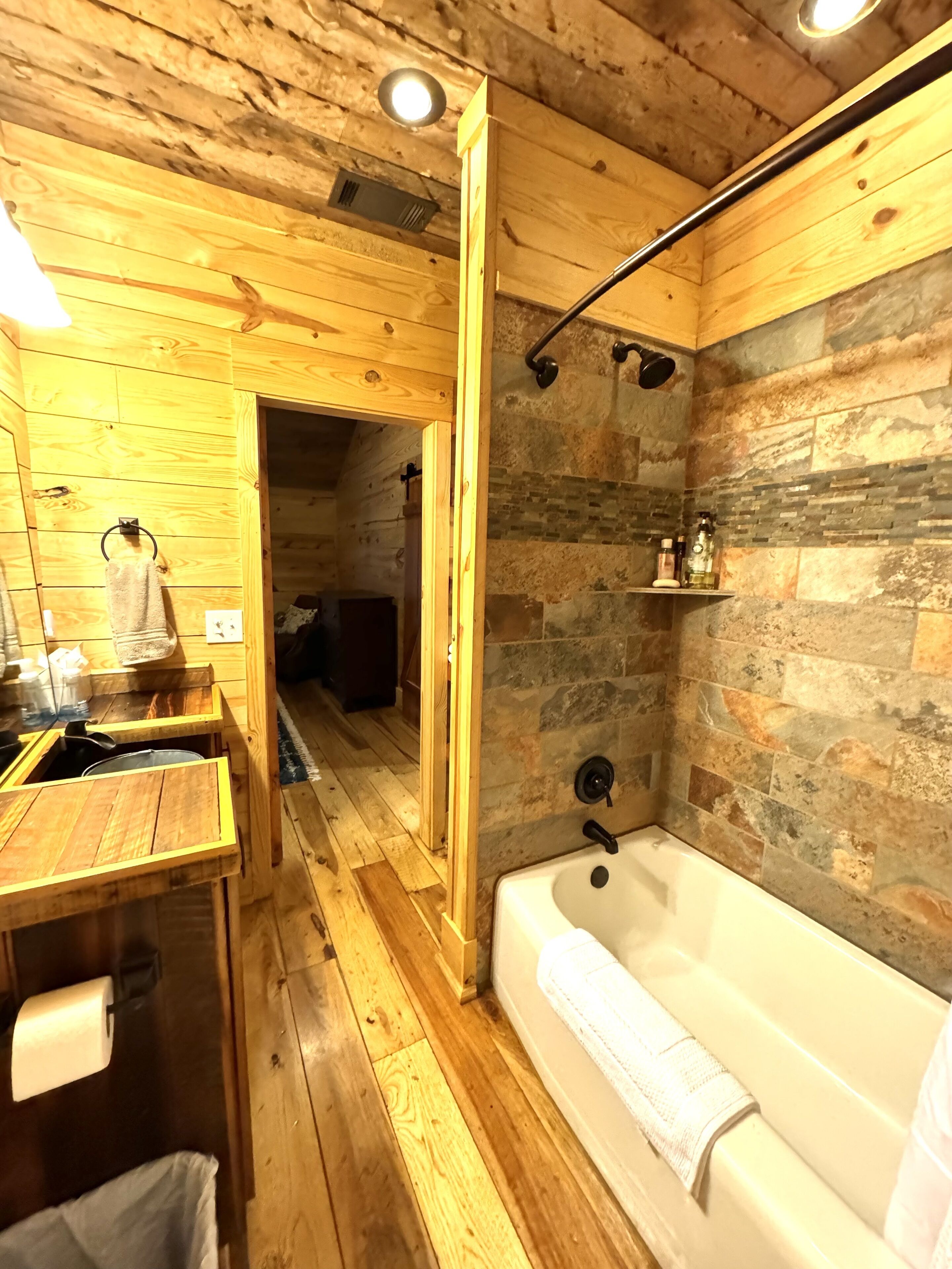 A wooden cabin bathroom with a bathtub, a wooden vanity, and a stone wall.
