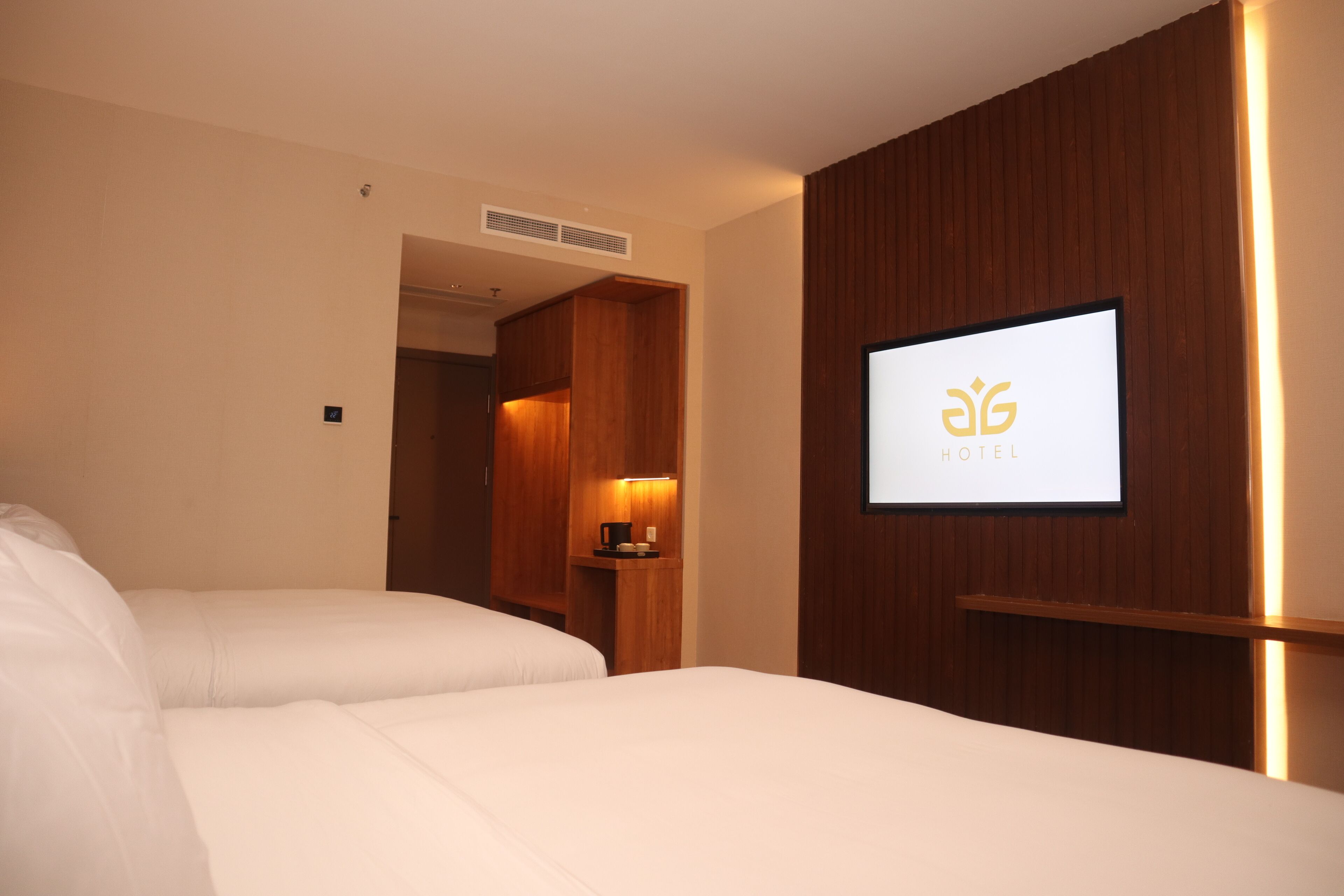 A hotel room with two beds, a wooden panel wall, a mounted TV, and a small table with a coffee maker.
