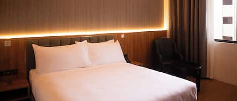 Habitación de hotel con una cama grande, una silla, una mesita y un ventanal con cortinas.