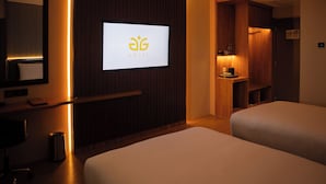Een hotelkamer met een bed, een bureau, een stoel, een prullenbak en een televisie waarop het logo van het hotel wordt weergegeven.