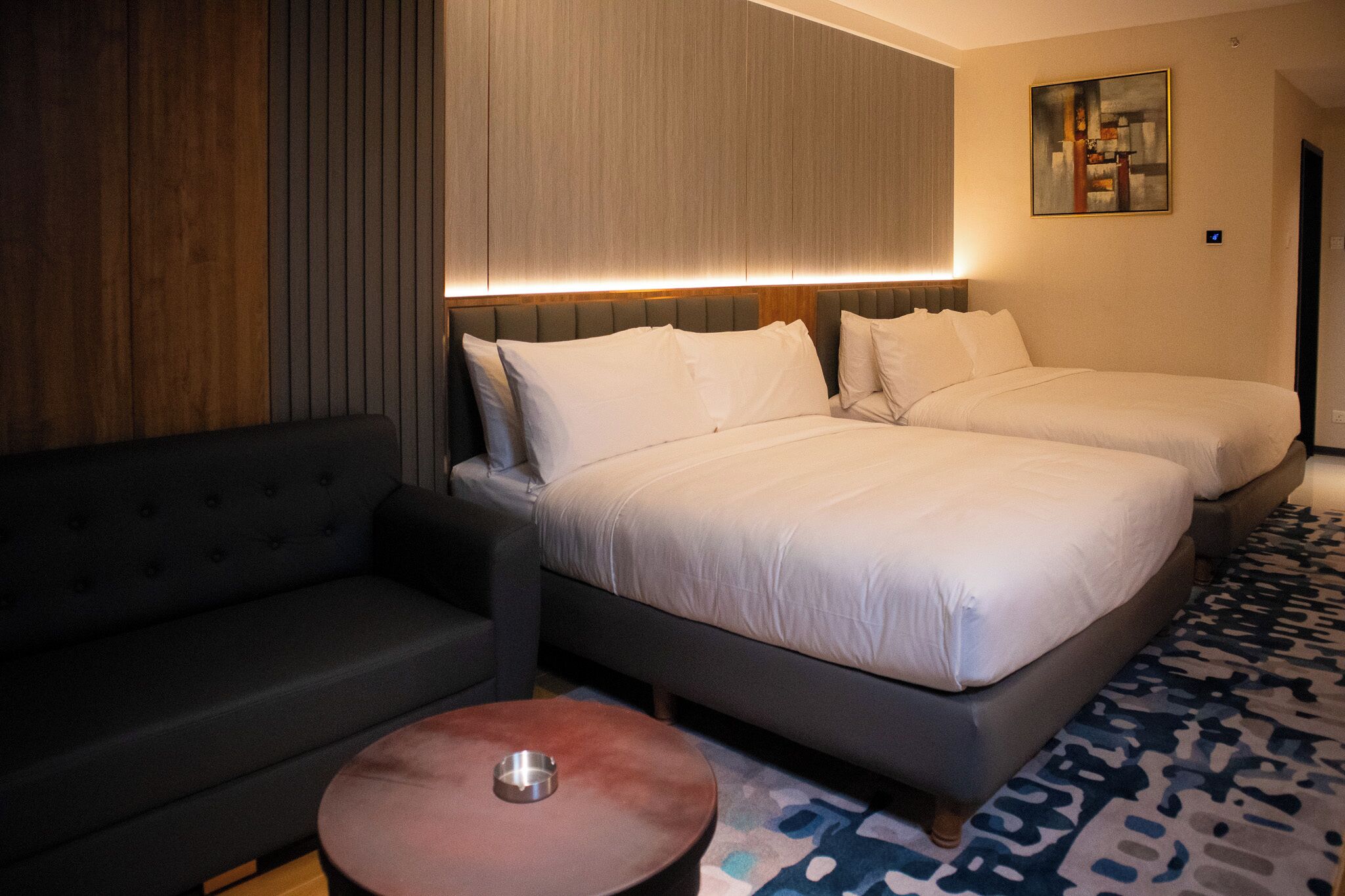 Een hotelkamer met twee bedden, een bank, een klein rond tafeltje en een schilderij aan de muur.