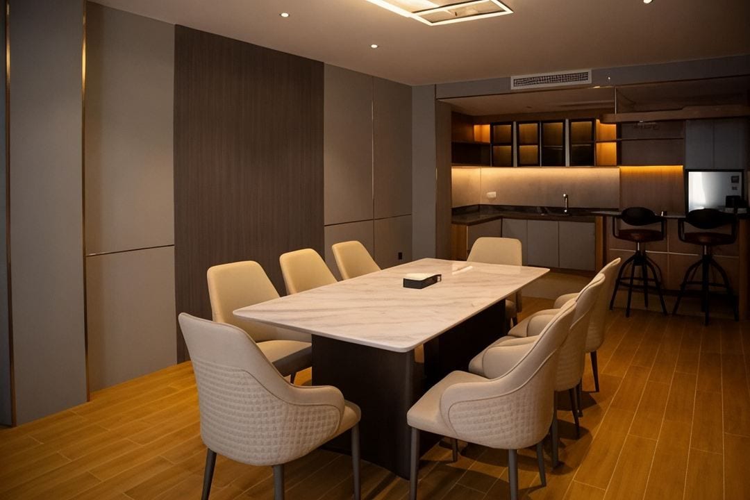 Un espace repas moderne avec une table rectangulaire et six chaises, une cuisine dotée d’un plan de travail foncé et de meubles éclairés, et un plancher en bois.