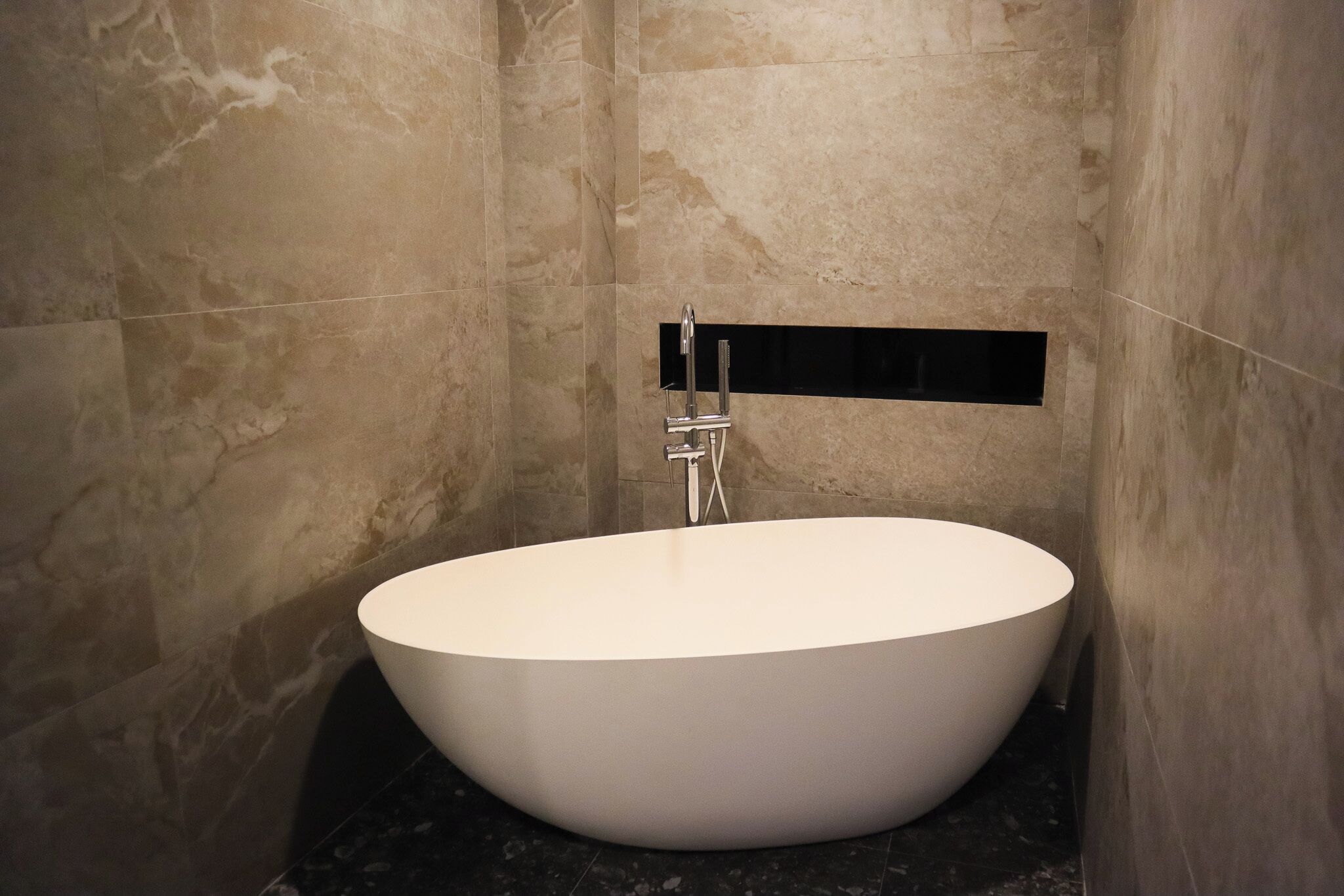 A modern bathroom with a freestanding bathtub, marble walls, and a black countertop.