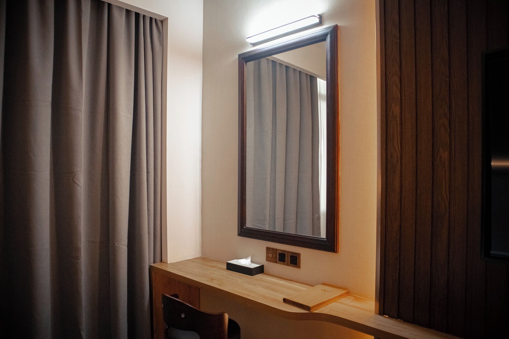 A hotel room with a wooden desk, a mirror, and a light above it.