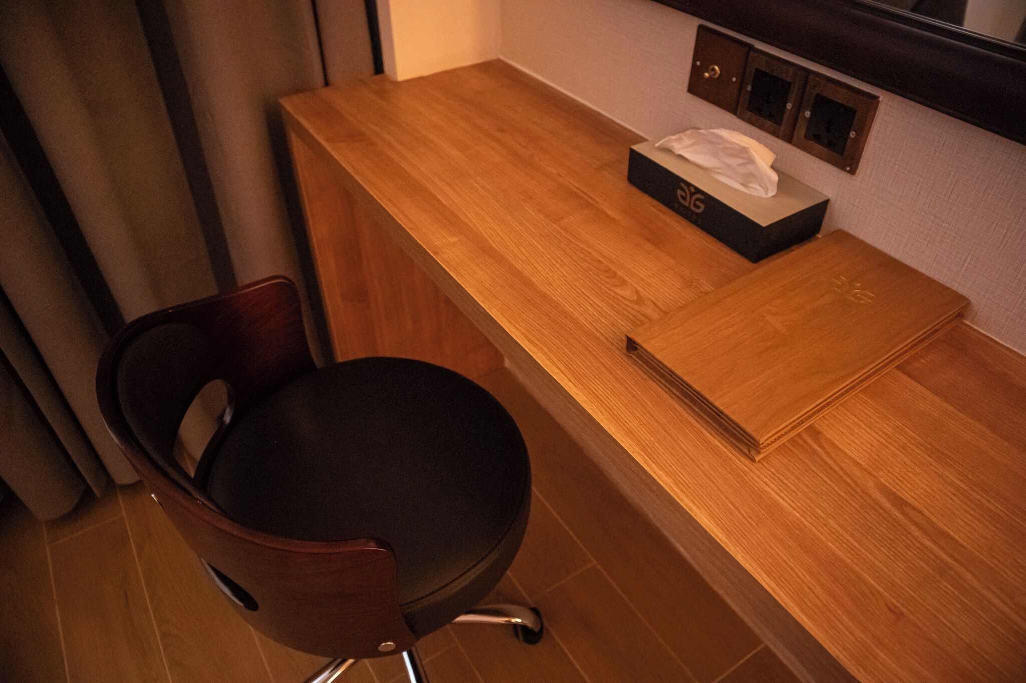 Un escritorio de madera con una caja de pañuelos, una silla y un espejo en la pared.