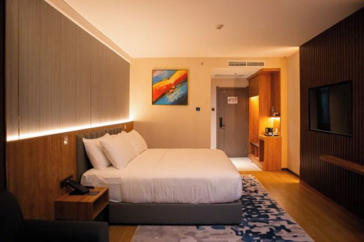 A hotel room with a bed, bedside table, lamp, and a painting on the wall.