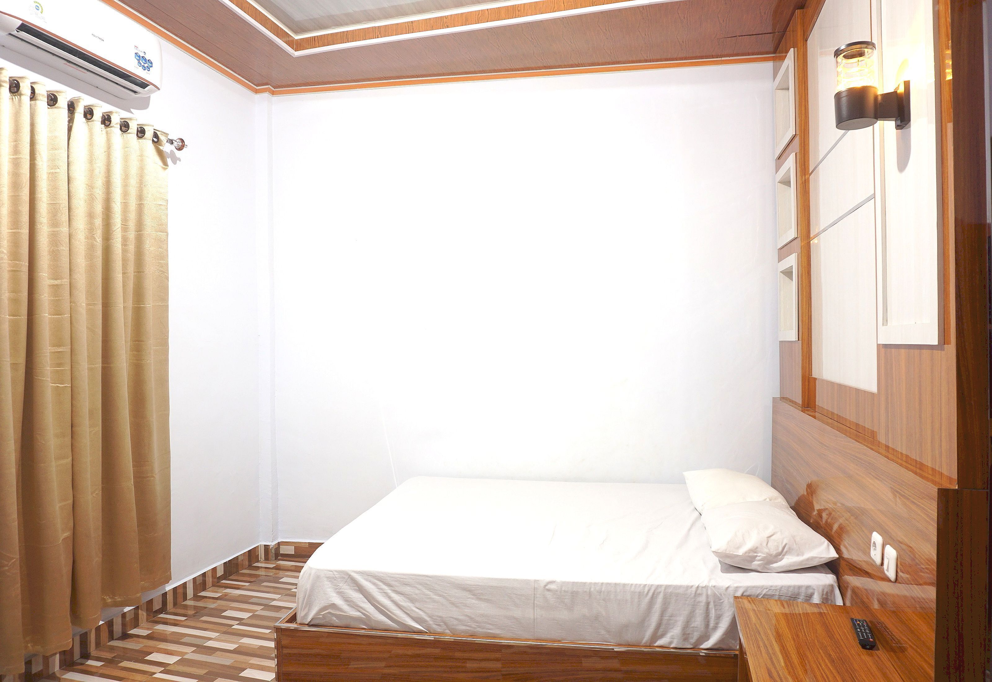 A small, neatly arranged bedroom with a bed, a wooden headboard, a bedside table, and a wall-mounted light fixture.