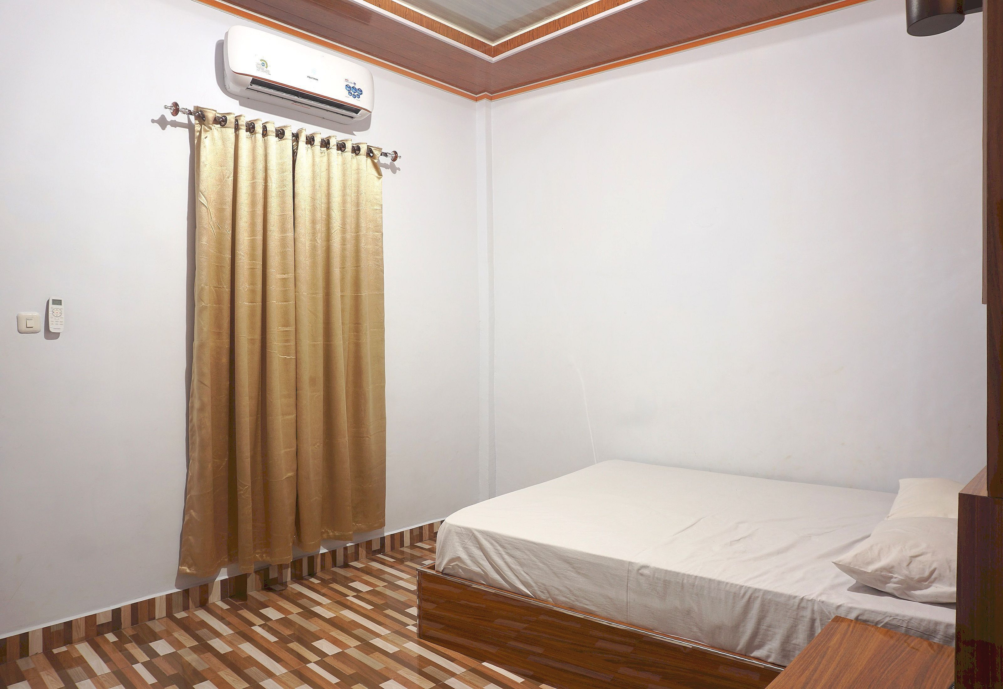 Une petite pièce propre, avec un lit simple, un plancher en bois, un rideau et un appareil de climatisation.