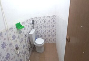 Um banheiro pequeno com vaso sanitário, uma lixeira verde e chuveiro.