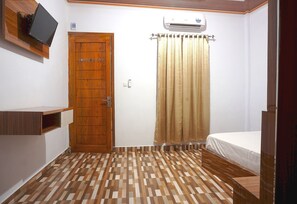 Quarto com porta de madeira, televisão na parede, ar condicionado, cama e piso estampado.