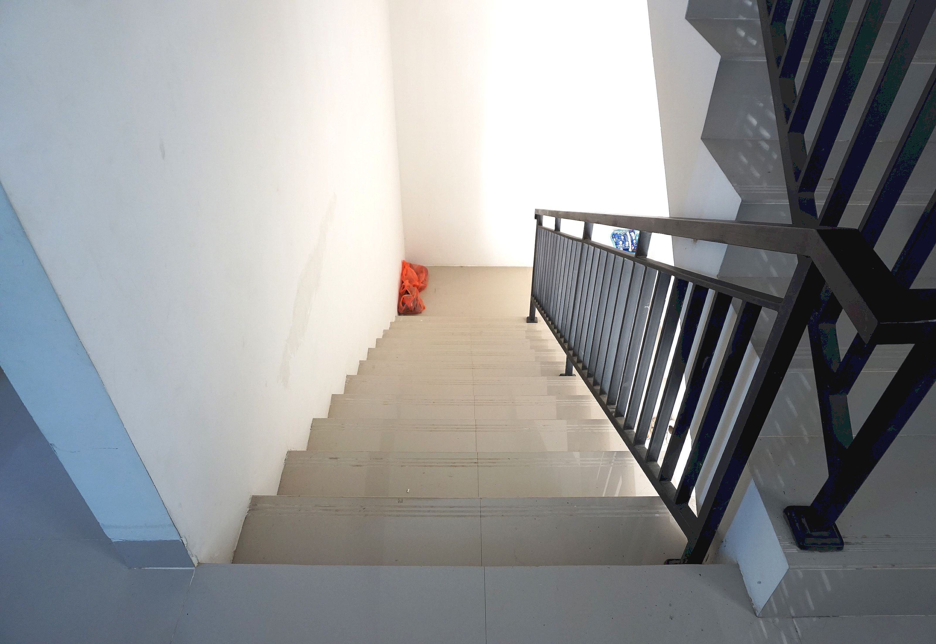 A staircase with a metal railing and a red bag on the floor.