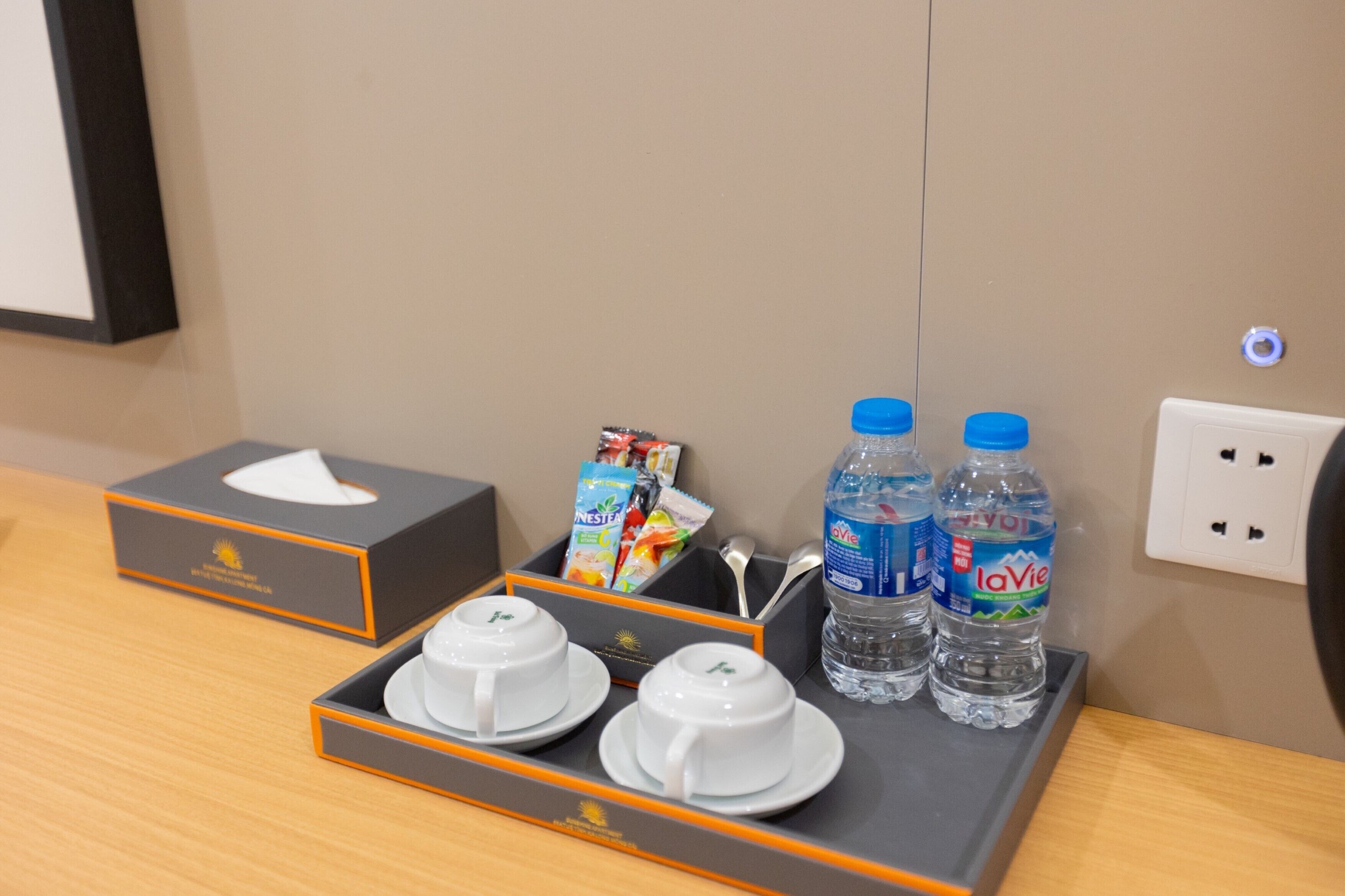 A hotel room's breakfast setup with a tray containing two white cups, two bottles of water, and a box of tissues.