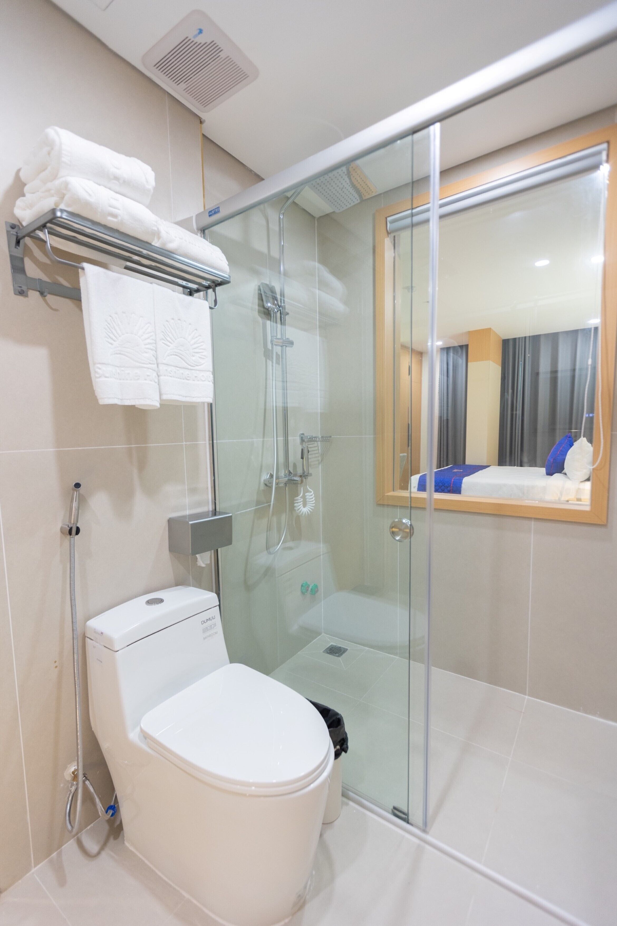 Un baño moderno con ducha de vidrio, inodoro y toallero con toallas dobladas.