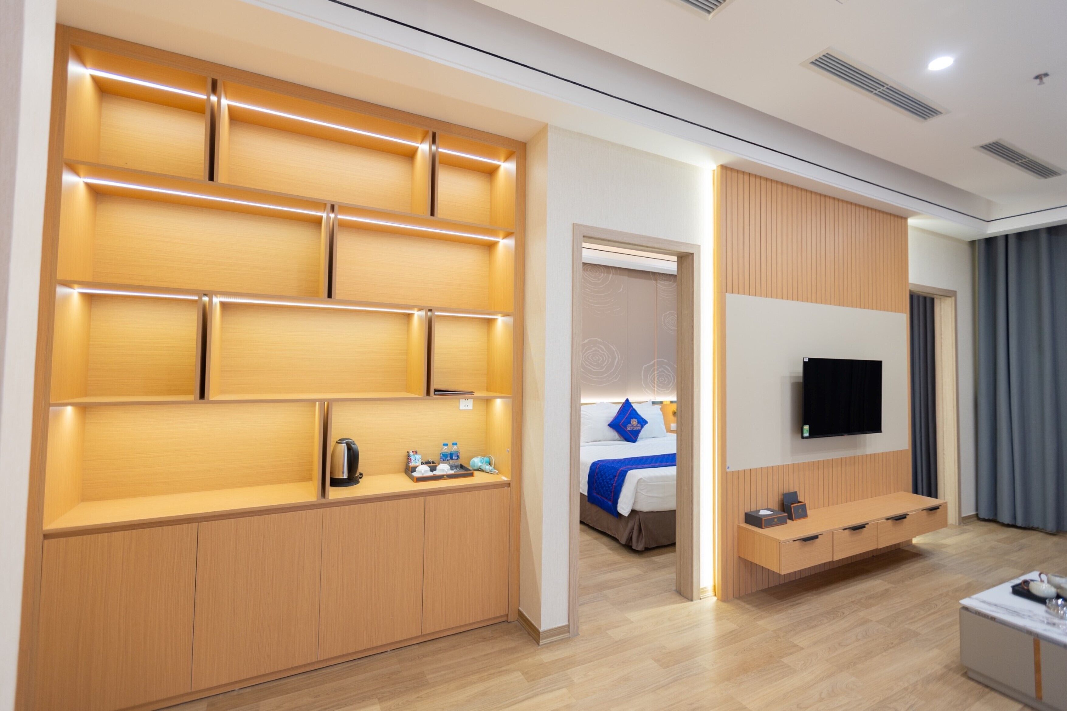 A modern hotel room with a wooden cabinet, a bed, a TV, and a small table.