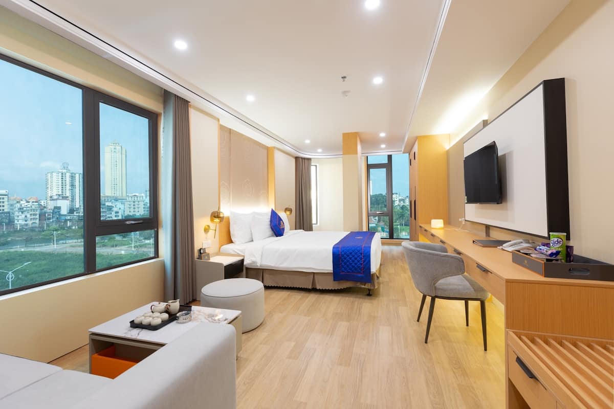 Ein modernes Hotelzimmer mit einem großen Bett, einem Schreibtisch, einem Sessel, einem Fernseher und Blick auf die Stadt.