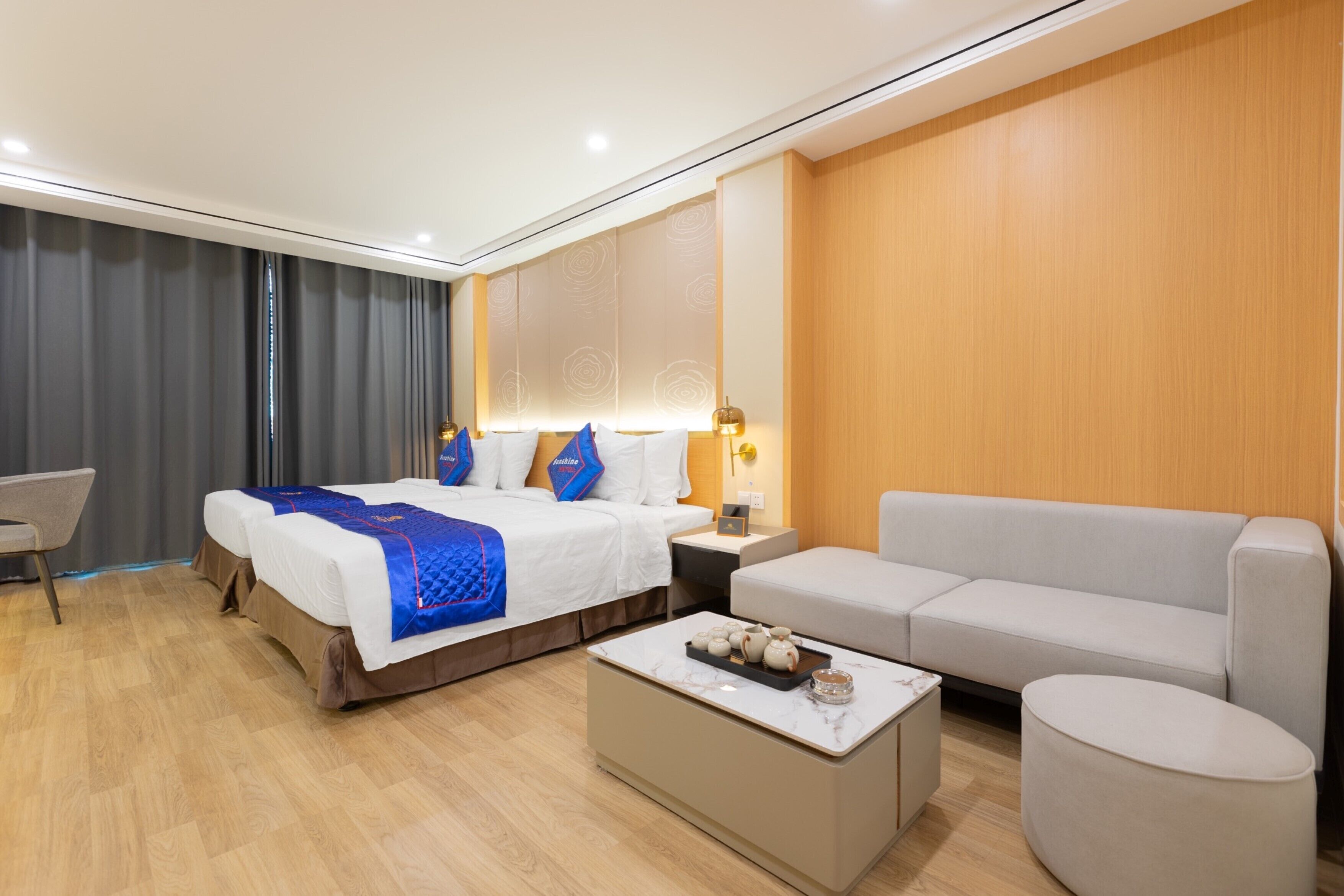 A modern hotel room with a large bed, a sofa, a coffee table, and a desk.