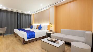 A modern hotel room with a large bed, a sofa, a coffee table, and a desk.