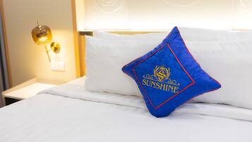 A neatly made bed with a white comforter and a blue pillow with "SUNSHINE" embroidered on it.