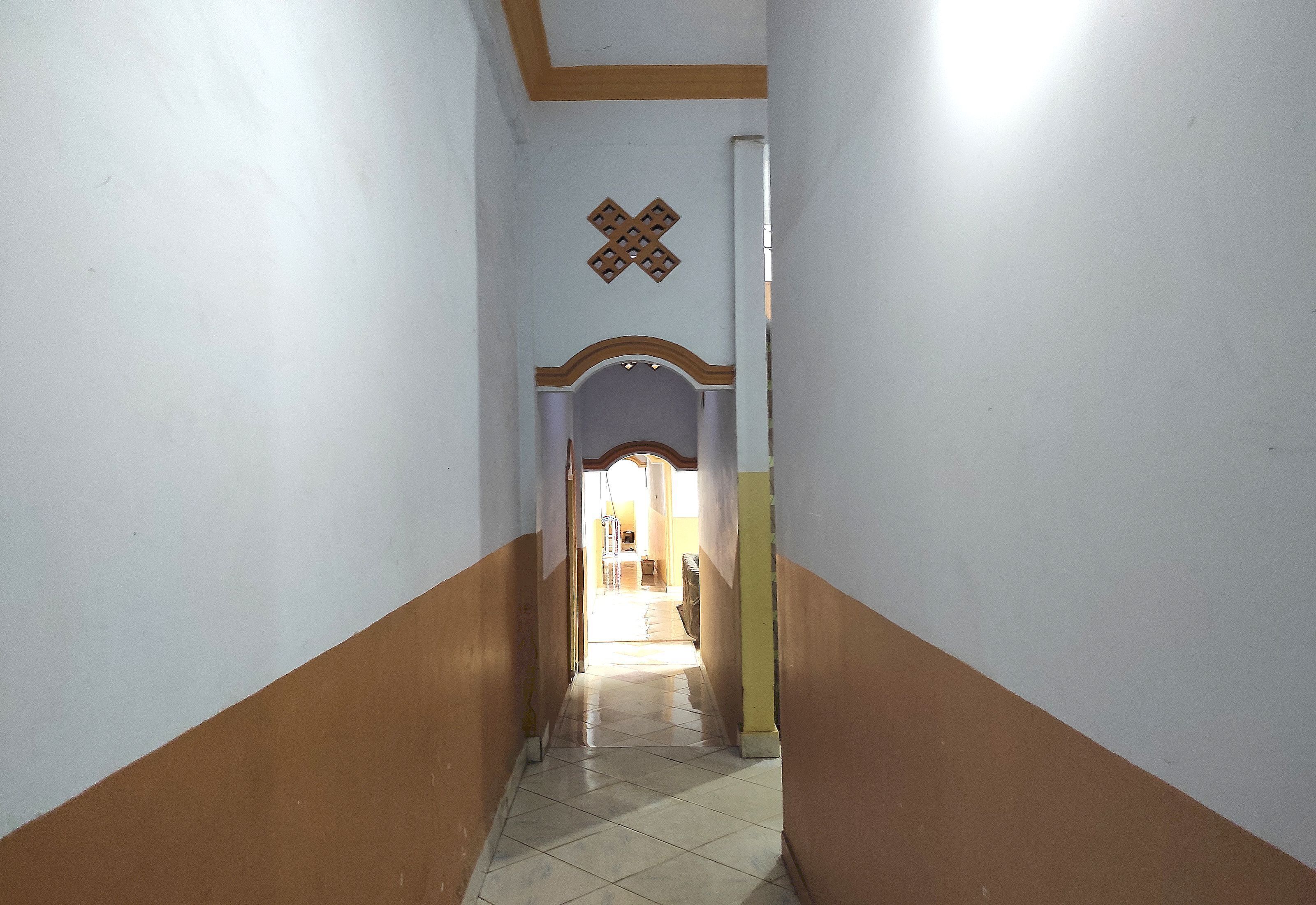 A narrow hallway with a tiled floor, white walls with brown trim, and a decorative wall pattern.