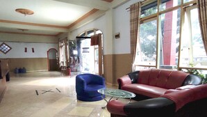 A lobby with a red and black sofa, a blue armchair, and a glass coffee table. - Hotel O Pondok Bintang (Kendari)